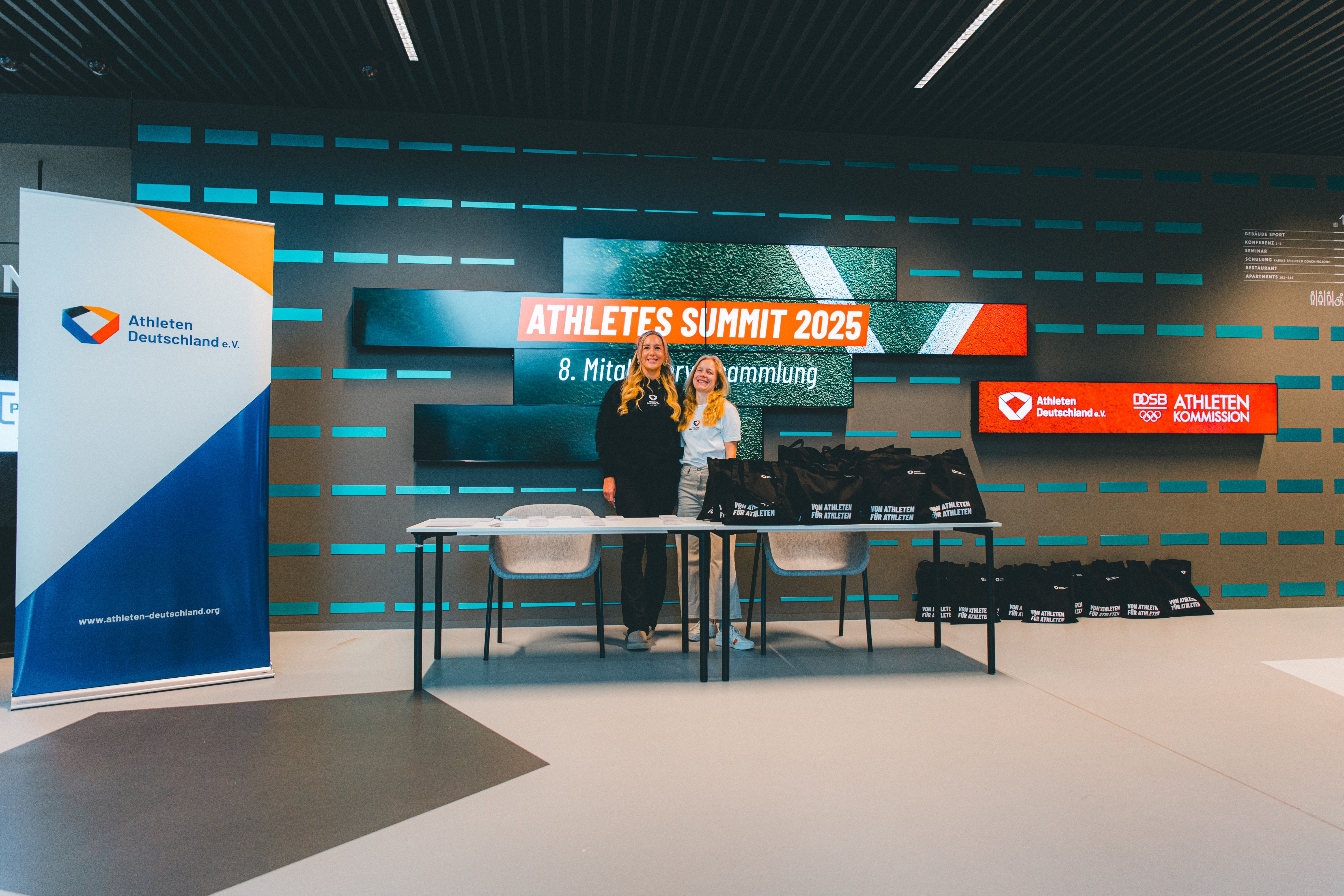 Zwei Mitarbeiterinnen von Athleten Deutschland stehen am Anmelde-Stand für die Mitgliederversammlung 2025.